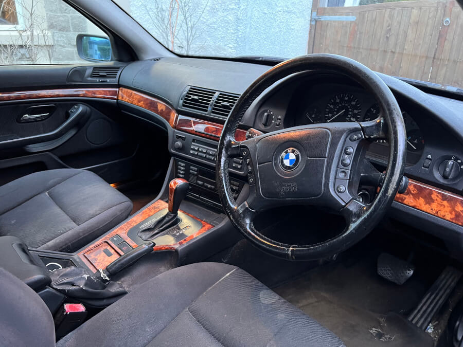 The interior of Andrew Scott’s BMW showcases a worn leather steering wheel, wood-trimmed dashboard, and aged upholstery, highlighting years of use and its role in his entrepreneurial story.